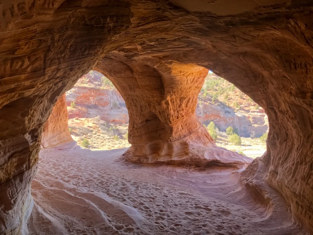 Grillige zandsteenbogen in het interieur van Moqui Cave met uitzicht op rode rotsen buiten