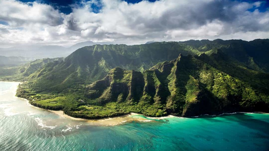 Luchtfoto van de groene, gekartelde kliffen van Kauai die uitkijken over een turquoise zee met golvende branding
