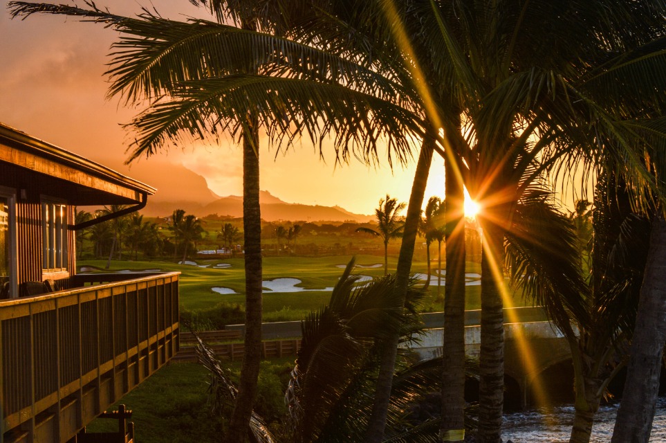 Zonsondergang tussen palmbomen met uitzicht op een golfbaan en bergen op Kauai, Hawaii