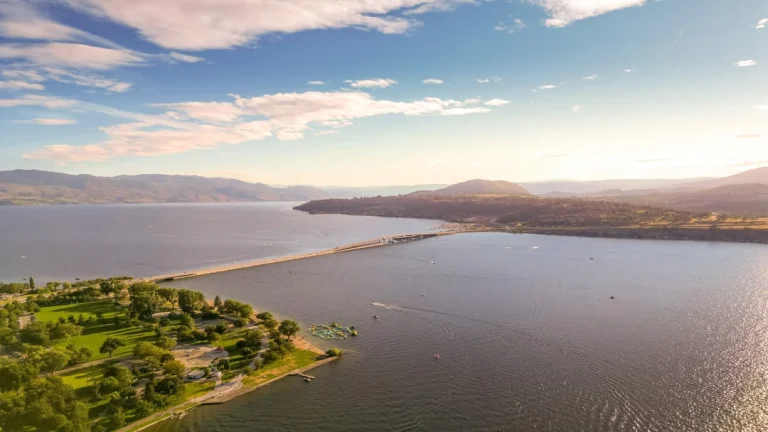 Luchtfoto van de brug over het Okanagan meer bij Kelowna, omringd door groene heuvels en een zonnig park aan de oever