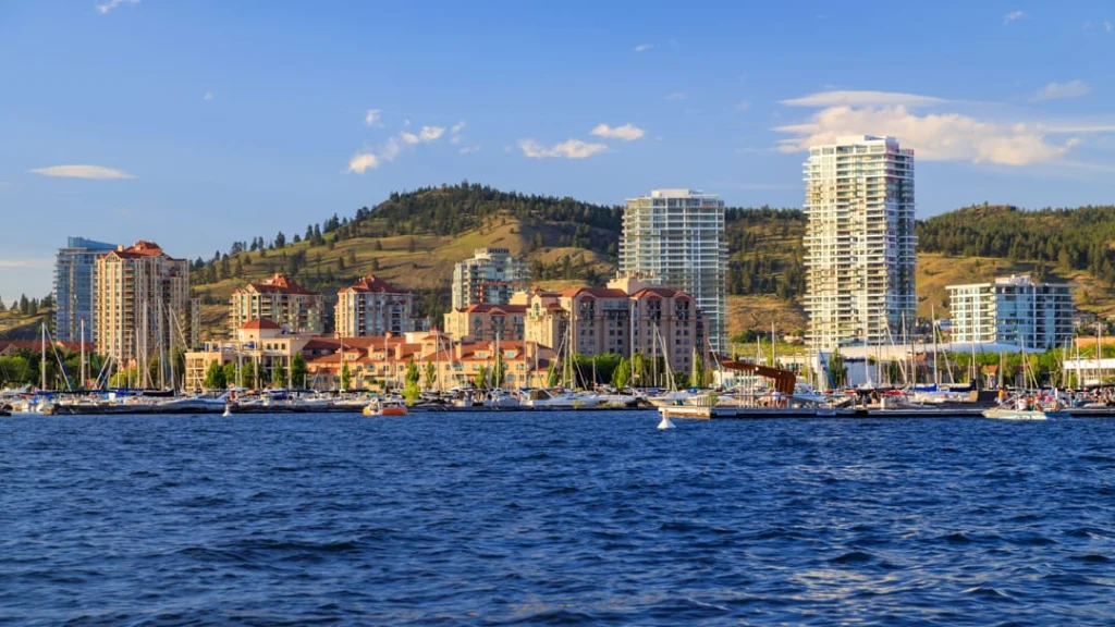 Zicht op de jachthaven en skyline van Kelowna met hoge appartementengebouwen en glooiende heuvels op de achtergrond