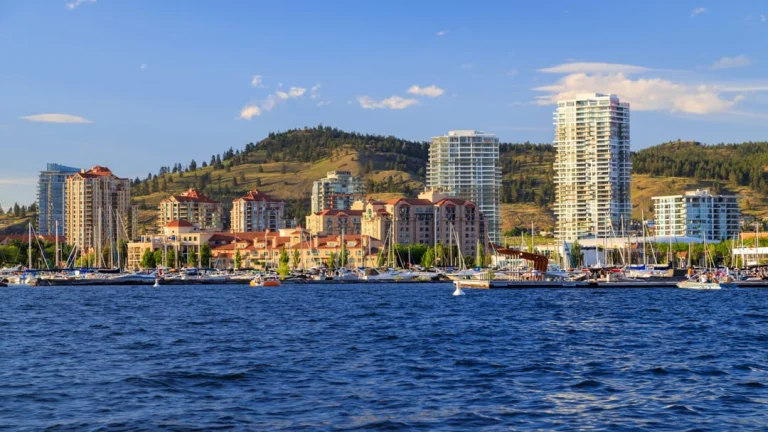 Zicht op de jachthaven en skyline van Kelowna met hoge appartementengebouwen en glooiende heuvels op de achtergrond