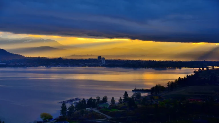 Gouden zonsondergang met dramatische wolkenlucht boven Okanagan Lake en de skyline van Kelowna in British Columbia