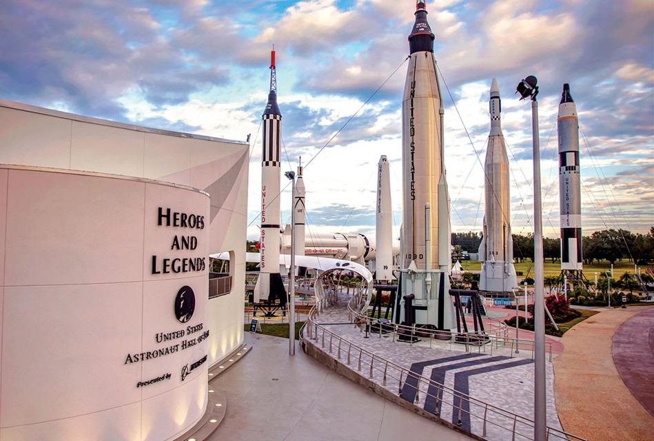 Wit museumgebouw met de tekst Heroes and Legends naast een rij hoge historische raketten tegen een bewolkte lucht