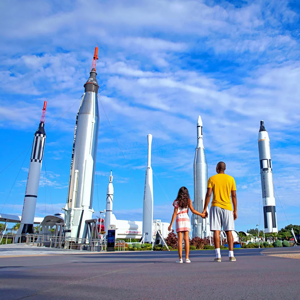 Vader en dochter kijken hand in hand omhoog naar een rij historische raketten in de Rocket Garden