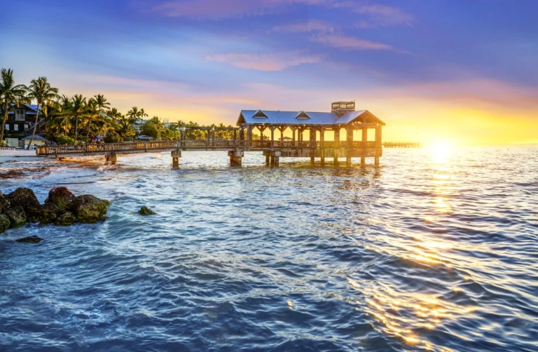 Een houten pier steekt uit in zee bij Key West terwijl de zon net boven de horizon opkomt en het water goud kleurt
