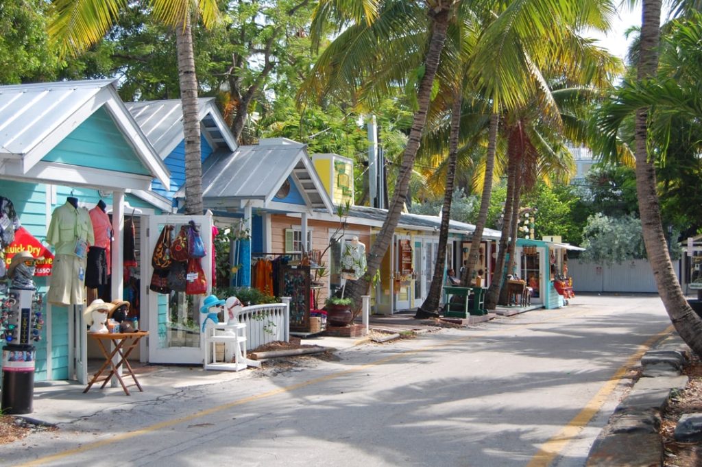 Rij kleine kleurrijke winkeltjes met kleding en souvenirs onder hoge palmbomen langs een rustige straat in Key West