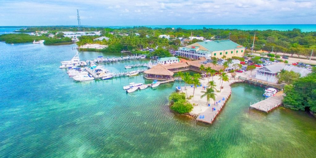 Luchtfoto van een jachthaven met aangemeerde boten, een groen gebouw en een klein schiereiland met palmbomen in Key West
