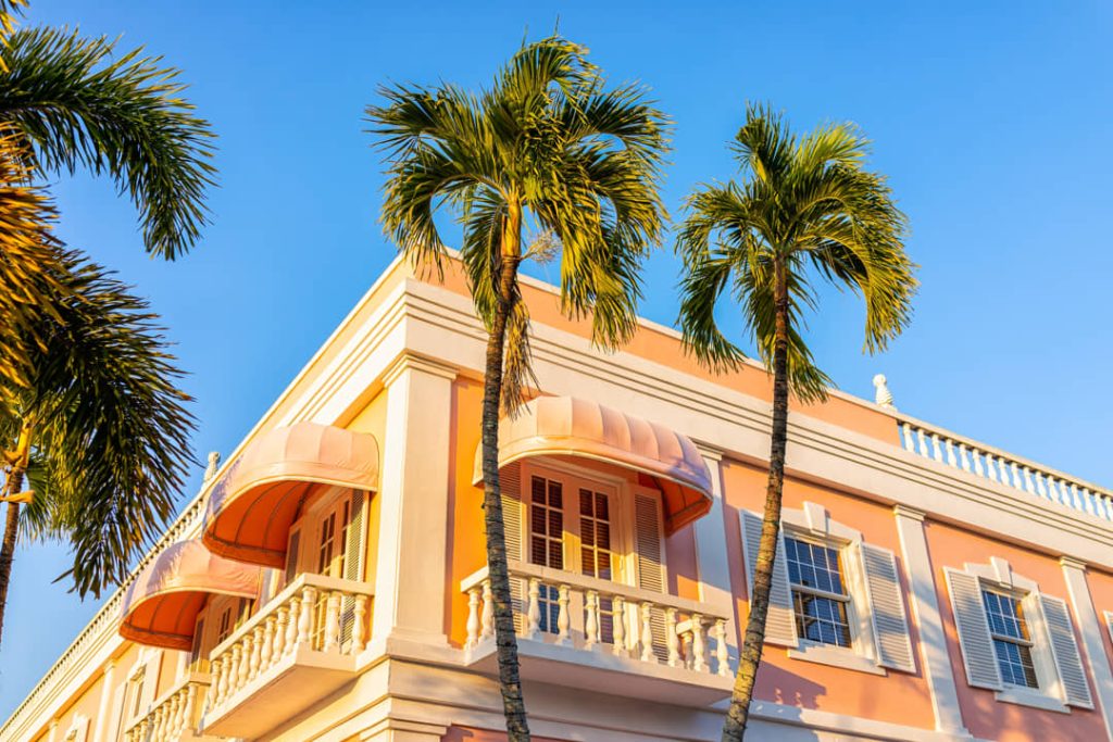 Roze gebouw met witte balkons en luiken tussen hoge palmbomen onder een strakblauwe hemel in Key West