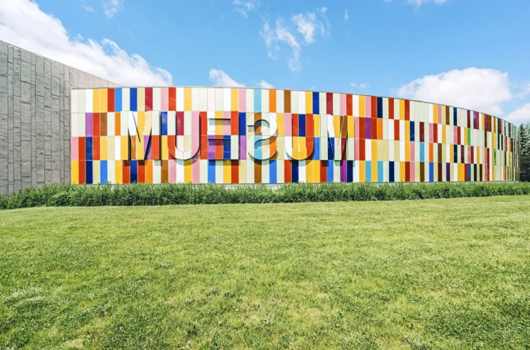 Gebogen gevel van gekleurde glazen panelen met de tekst museum erin verwerkt, voor een groen grasveld in Kitchener