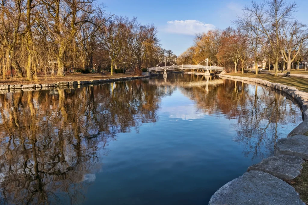 Rustige vijver met een wit bruggetje omringd door kale bomen in een stadspark in Kitchener op een zonnige winterdag