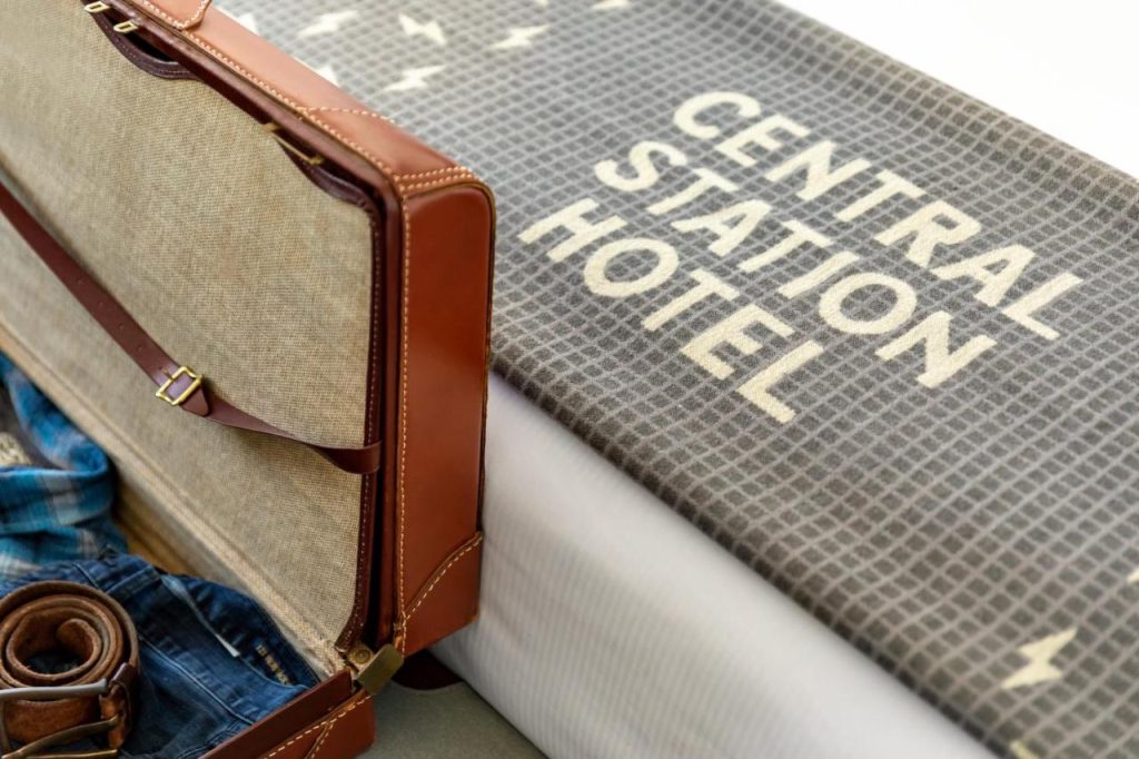 Opengeklapte leren koffer met kleding naast een bedsprei met de tekst Central Station Hotel