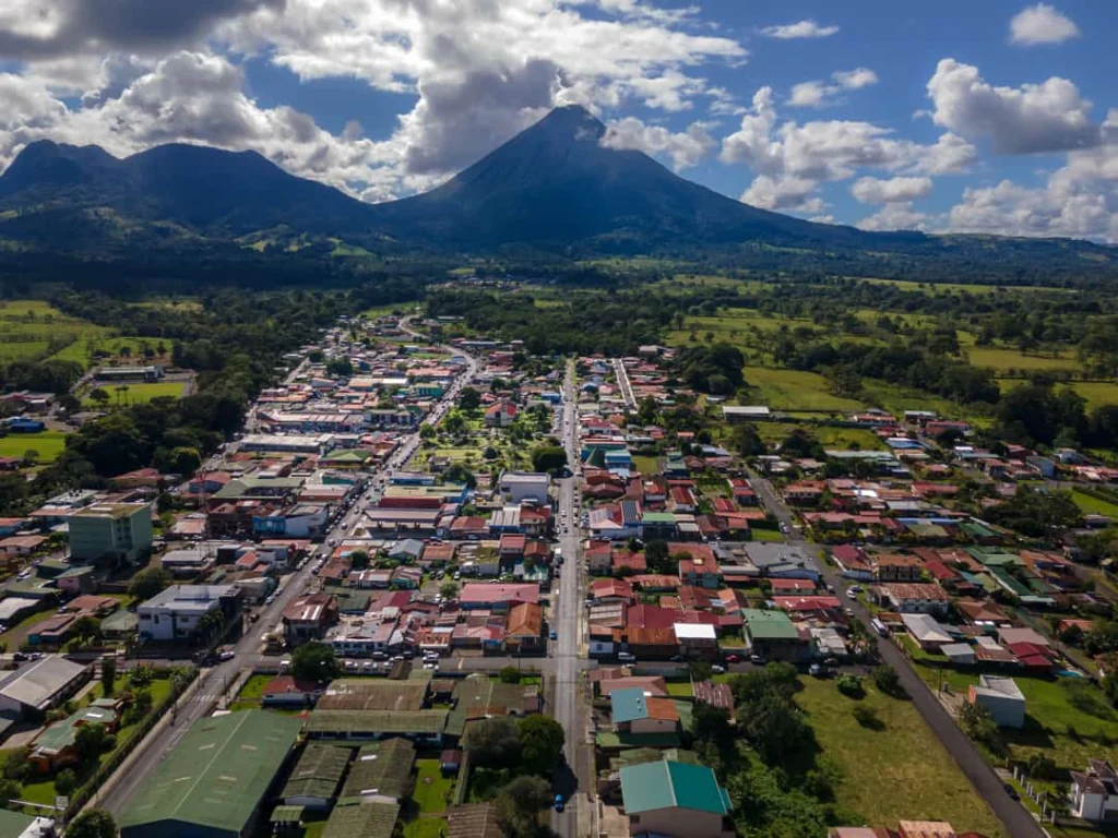 Luchtfoto van het dorp La Fortuna met een lange hoofdstraat en daken, met de kegelvormige Arenal-vulkaan op de achtergrond in Costa Rica