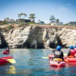 Groep kajakkers met helm en zwemvest peddelt in rode kajaks langs de kalkstenen kustgrotten van La Jolla in Californië