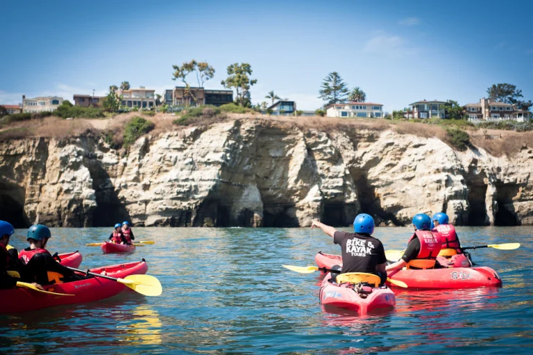 Groep kajakkers met helm en zwemvest peddelt in rode kajaks langs de kalkstenen kustgrotten van La Jolla in Californië