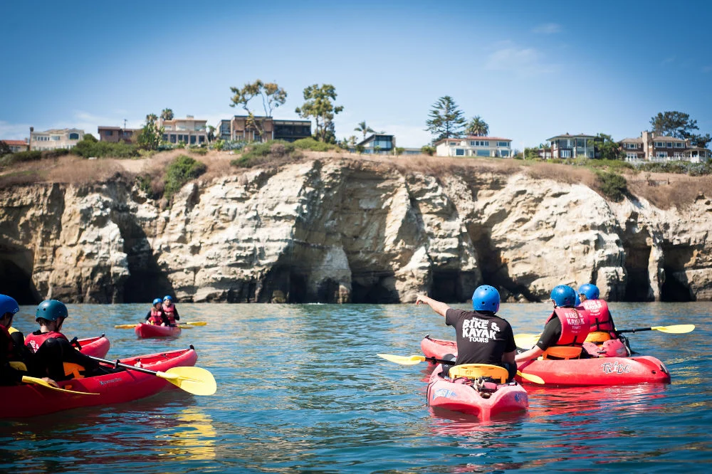 Groep kajakkers met helm en zwemvest peddelt in rode kajaks langs de kalkstenen kustgrotten van La Jolla in Californië