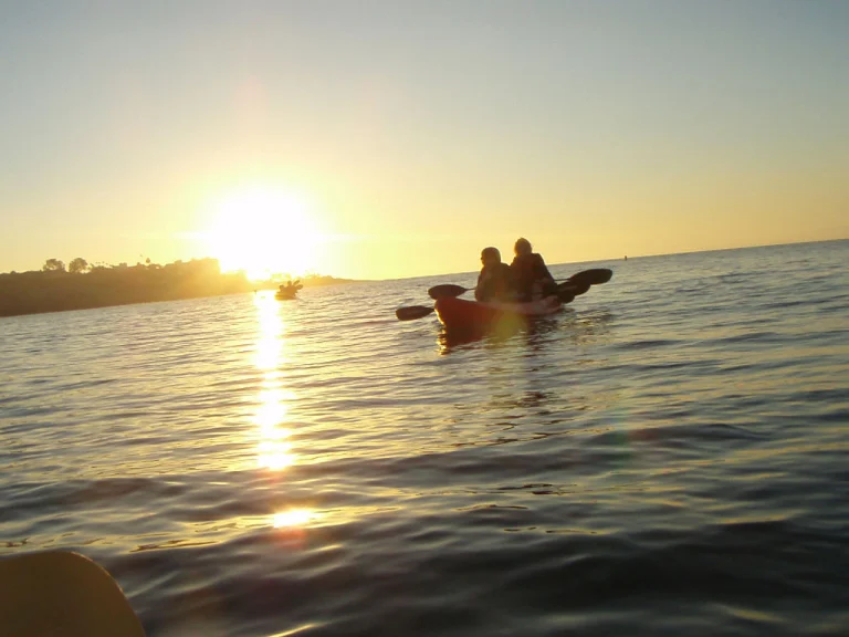 Twee kayakvaarders peddelen op zee terwijl de zon laag boven de kustlijn van La Jolla ondergaat