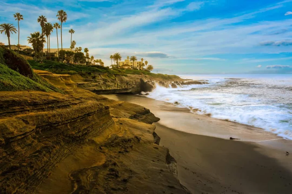 Verweerde zandstenen kliffen langs de kustlijn van La Jolla in San Diego met schuimende golven bij zonsondergang
