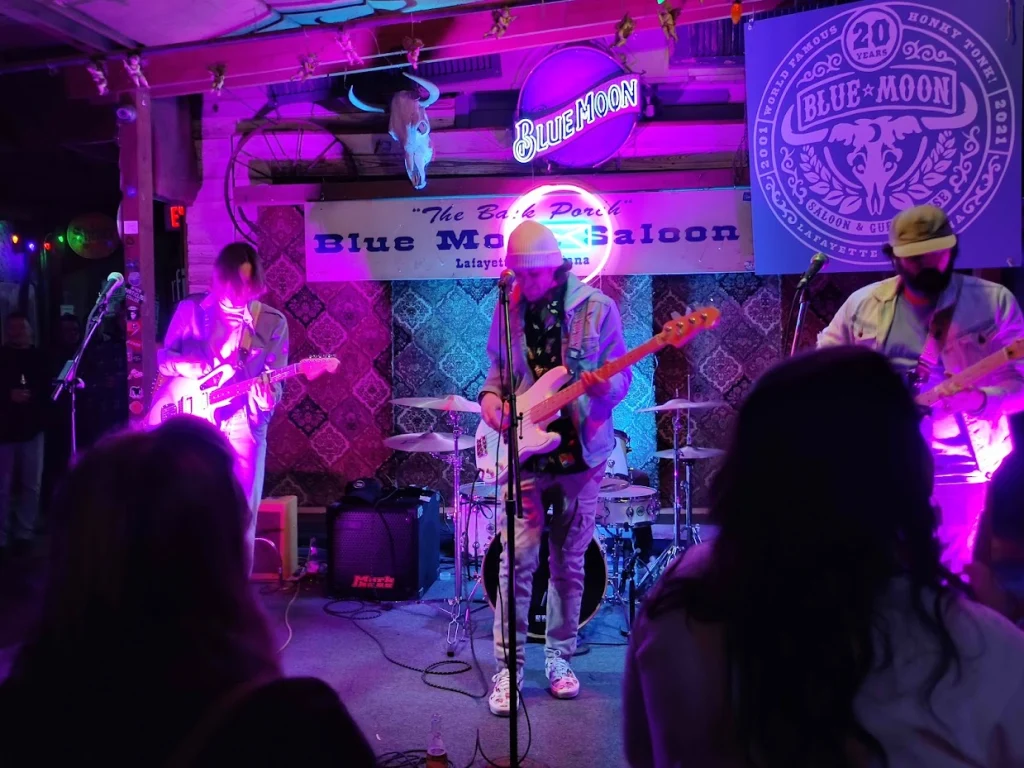 Band met gitaristen speelt live op een klein podium met paars licht in de Blue Moon Saloon in Lafayette in Louisiana, publiek op de voorgrond