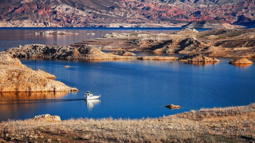Klein wit bootje vaart over het kalme blauwe water van Lake Mead tussen kleine rotsachtige eilandjes en droge oevers