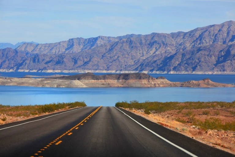 Rechte tweebaansweg door de woestijn die uitkomt op het blauwe water van Lake Mead met kale bergen op de achtergrond