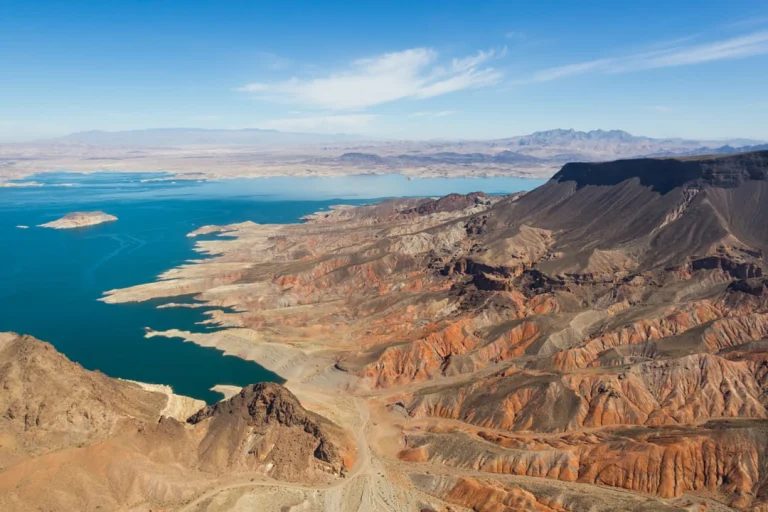 Luchtfoto van Lake Mead met turkoois water naast roodbruin geerodeerde rotsformaties en bergen in de verte