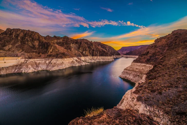 Kleurrijke lucht met oranje en roze tinten boven een rotsachtige kloof met kalm donker water van Lake Mead
