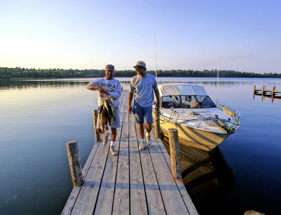 Twee vissers lopen met hun vangst over een steiger naar een boot bij een resort aan Lake of the Woods