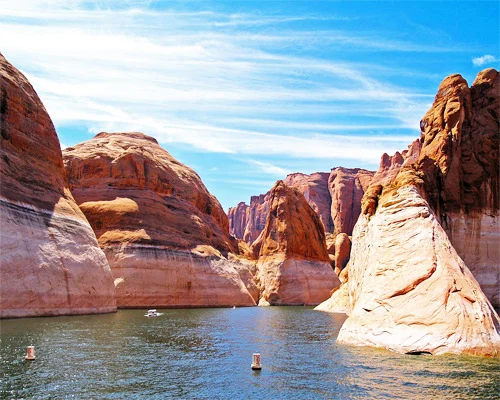 Smal kanaal van turquoise water tussen steile gestreepte zandsteenrotsen, met kleine boten in de verte op Lake Powell