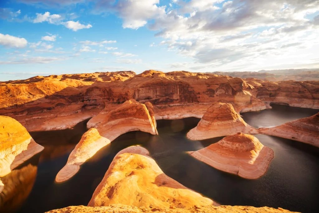 Gladde golvende zandstenen rotsformaties steken als schiereilanden in het donkere water van Lake Powell onder een bewolkte lucht