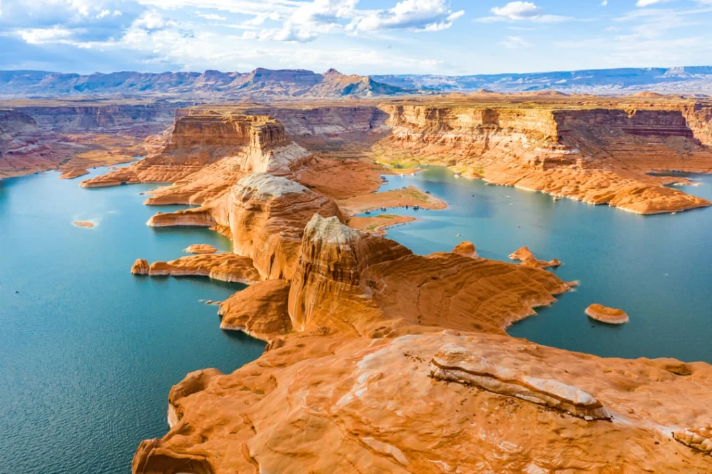 Luchtfoto van Lake Powell met hoge rode rotswanden die het heldere blauwe water omringen onder een wolkenlucht