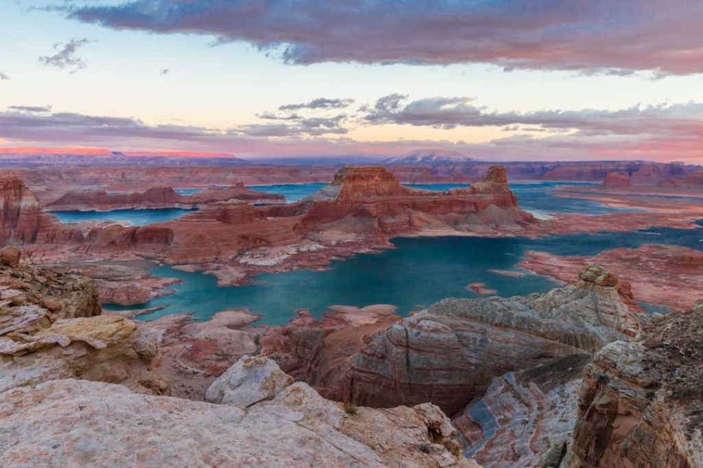 Luchtfoto van rood oplichtende rotsformaties die uit het turquoise water van Lake Powell steken onder een roze avondlucht