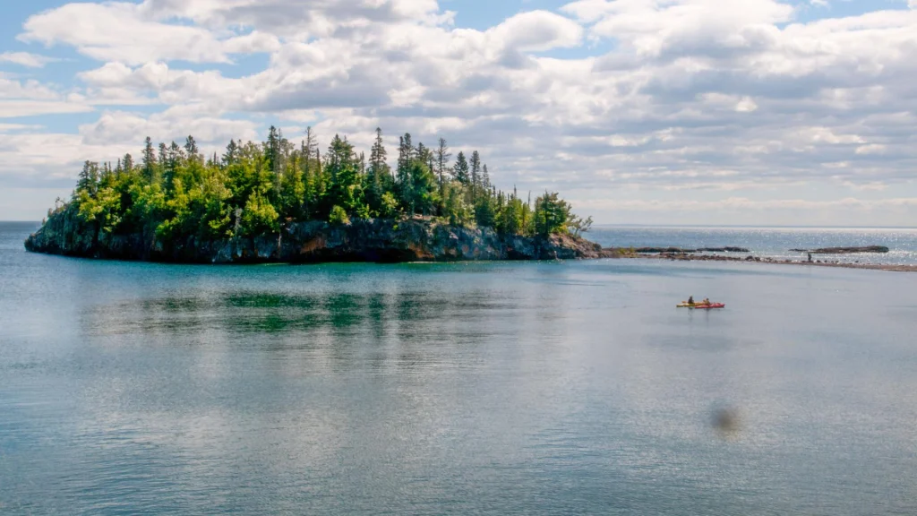 Twee kayakers peddelen op Lake Superior langs een klein rotsachtig eilandje met dennenbomen
