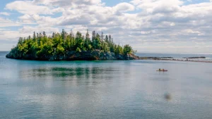 Twee kayakers peddelen op Lake Superior langs een klein rotsachtig eilandje met dennenbomen