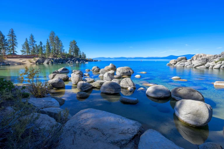 Grote gladde granietkeien liggen in het heldere turquoise water van Lake Tahoe met dennenbomen aan de oever