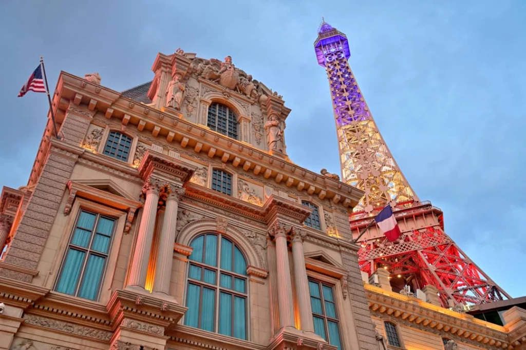 Verlichte replica van de Eiffeltoren naast de klassieke gevel van hotel Paris Las Vegas bij schemering