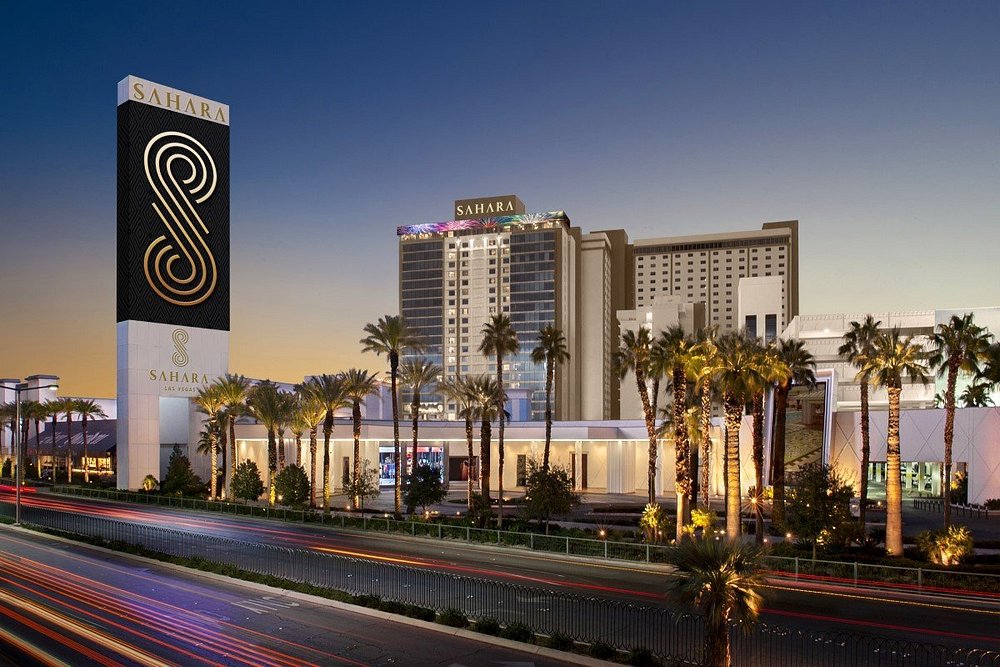 De verlichte toren en het bord van hotel Sahara steken uit boven de palmbomen in de avondschemering in Las Vegas