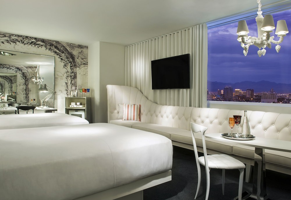 Een witte hotelkamer met een grote bank en televisie kijkt door het raam uit over de skyline van Las Vegas bij avond