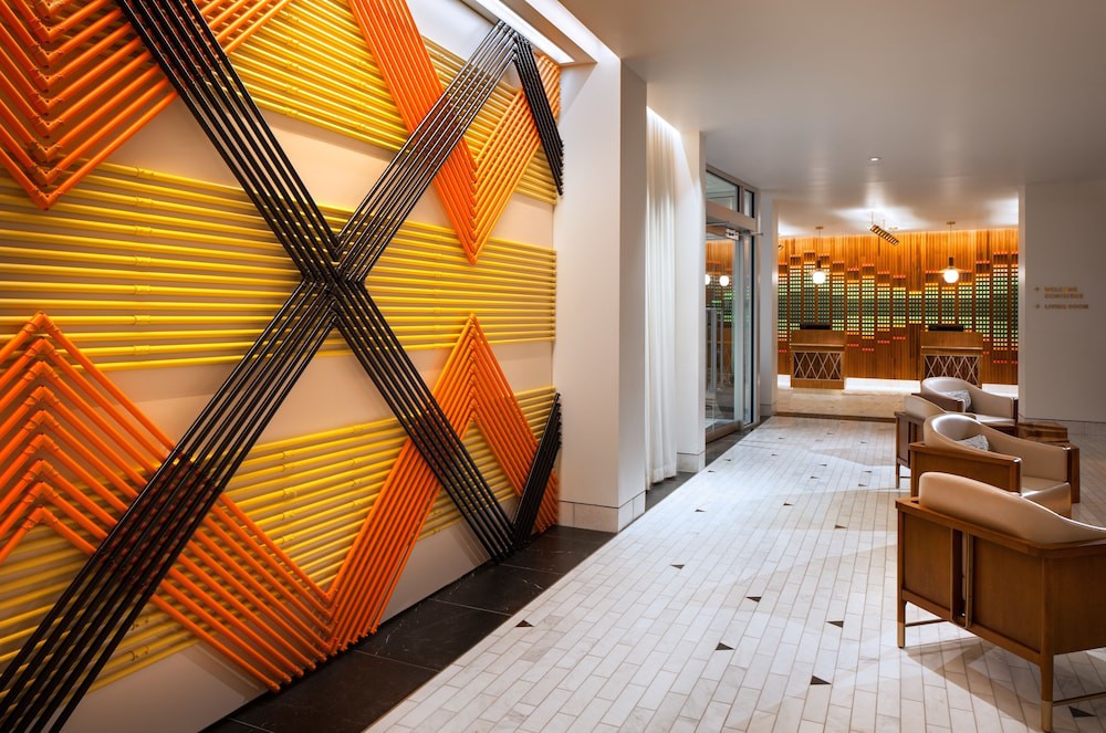 Een moderne hotellobby met een gele en oranje geometrische muurdecoratie en een lounge met fauteuils