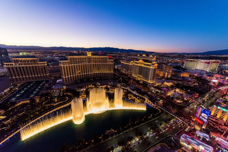 Luchtfoto bij schemering van de verlichte fonteinen van het Bellagio hotel met de Strip van Las Vegas op de achtergrond