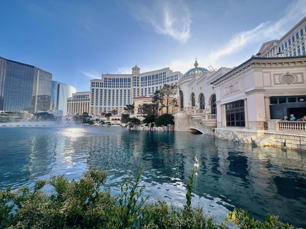 Wit hotelcomplex met een koepeltoren aan het water van het Bellagio meer, met wolkenkrabbers op de achtergrond onder een blauwe lucht