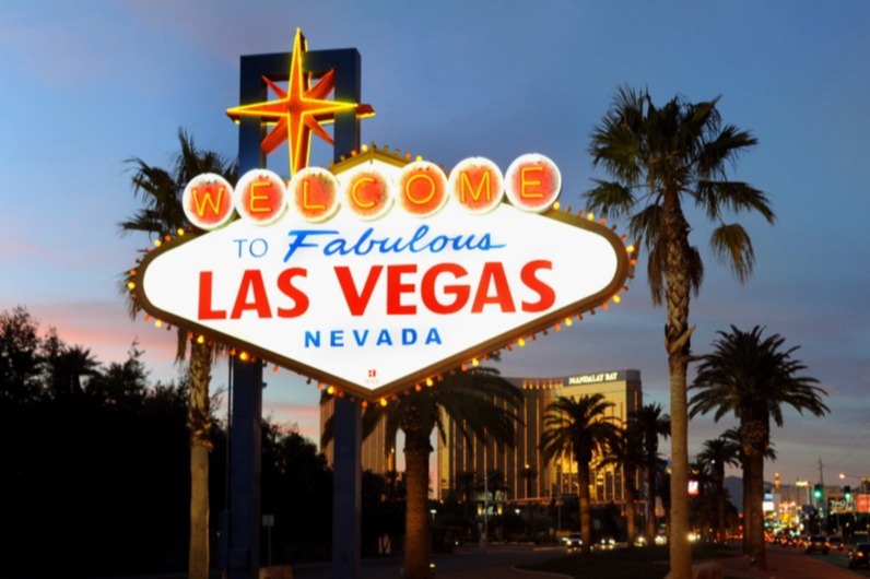 Verlicht diamantvormig bord met de tekst Welcome to Fabulous Las Vegas Nevada, met palmbomen en hotels op de achtergrond