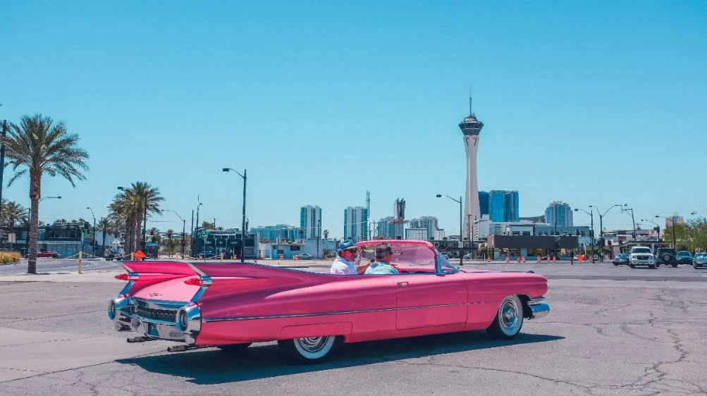 Glimmende roze klassieke Cadillac cabriolet geparkeerd in Las Vegas met palmbomen en de Stratosphere toren op de achtergrond
