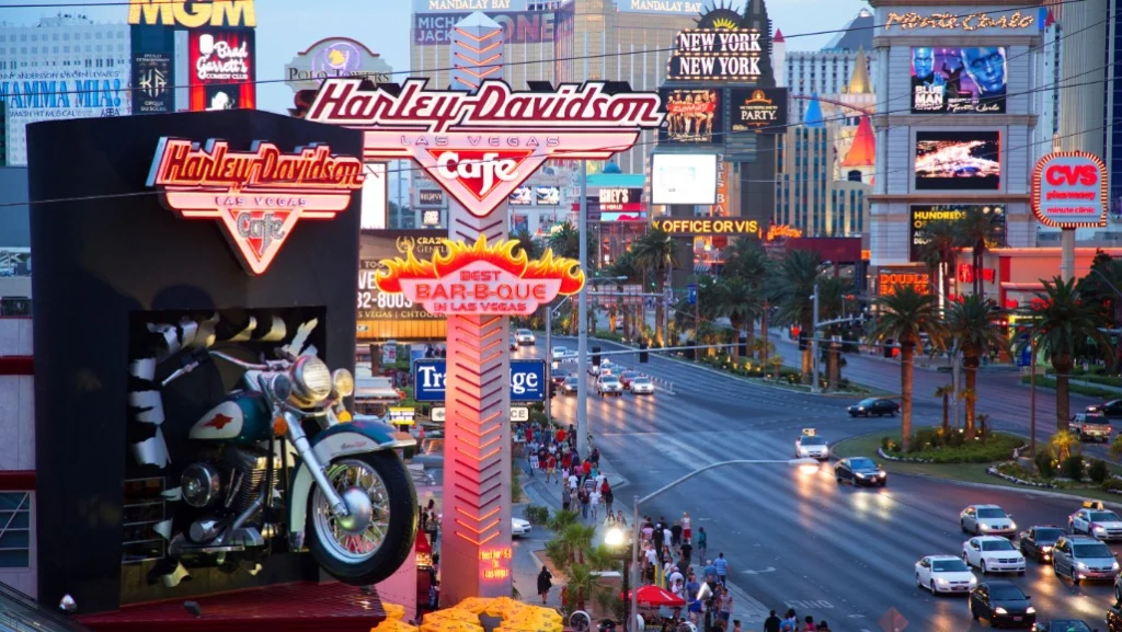 Drukke Las Vegas Strip in de avondschemering met felle neonreclames waaronder Harley Davidson Cafe en verkeer op de weg