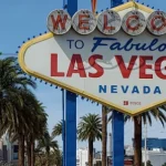 Het bekende Welcome to Fabulous Las Vegas bord tussen palmbomen met hotels van de Strip op de achtergrond bij daglicht