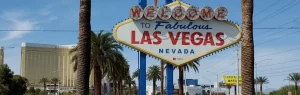 Het bekende Welcome to Fabulous Las Vegas bord tussen palmbomen met hotels van de Strip op de achtergrond bij daglicht