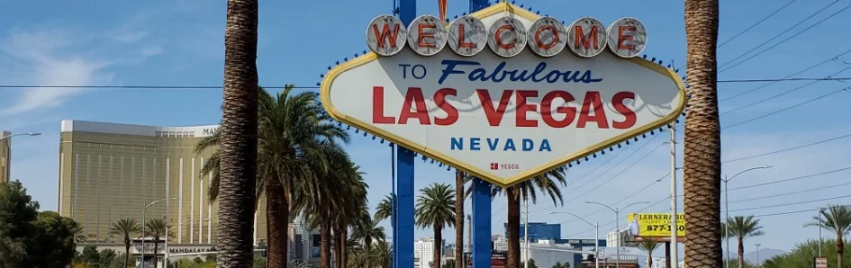 Het bekende Welcome to Fabulous Las Vegas bord tussen palmbomen met hotels van de Strip op de achtergrond bij daglicht