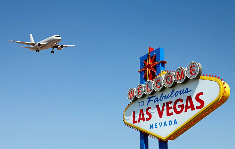 Vliegtuig nadert de landingsbaan boven het Welcome to Fabulous Las Vegas bord tegen een strakblauwe lucht