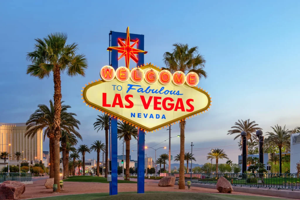 Het beroemde verlichte welkomstbord van Las Vegas tussen palmbomen bij het invallen van de avond