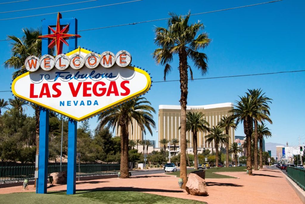 Het beroemde Welcome to Fabulous Las Vegas bord met palmbomen en een hotel op de achtergrond onder een strakblauwe lucht